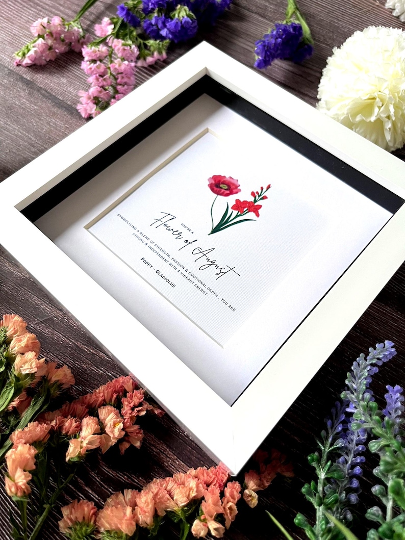 May include: A white framed print with a black mat. The print features a watercolor illustration of a poppy and gladiolus flower with the text "You're a Flower of August. Symbolizing a blend of strength, passion & emotional depth, you are strong & independent with a vibrant energy. Poppy - Gladiolus".