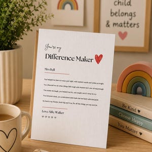 以下が含まれることがあります： You're my Difference Makerという黒い文字が書かれた白いグリーティングカード。Mrs Bell宛ての詩が続き、Love Alfie Walkerという署名と5つの小さなハートが描かれています。カードには赤いハートのグラフィックと質感のある紙の仕上げが施されています。