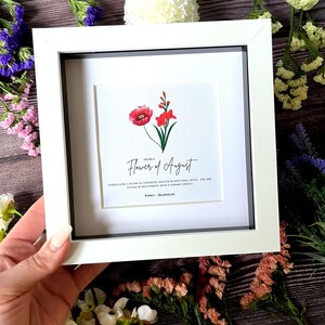 May include: A white framed print with a red poppy and a pink gladiolus flower. The text reads "You're a Flower of August. Symbolizing a blend of strength, passion & emotional depth. You are strong & independent with a vibrant energy. Poppy - Gladiolus"