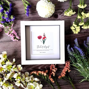 May include: White frame with a white mat and a print of a red poppy flower. The print has the text "Flower of August" and "Poppy - Glamorous".
