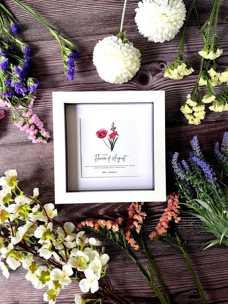 May include: White frame with a white mat and a print of a red poppy flower. The print has the text "Flower of August" and "Poppy - Glamorous".
