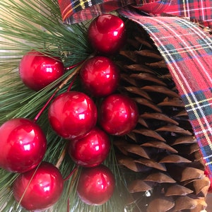May include: A close-up of a Christmas wreath with red ornaments, pine needles, and a plaid ribbon.