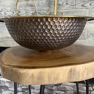 Custom made handmade brass sink: hammered copper bowl with rustic texture, tall luxe brass faucet on a wooden countertop.
