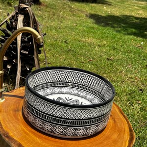 Round Moroccan ceramic vessel sink with hand-painted black-and-white geometric pattern and gold drain on a marble counter.