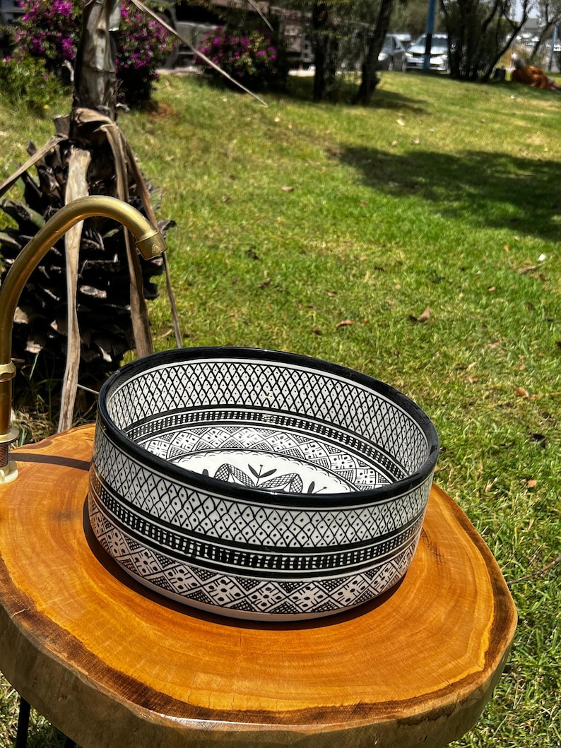Round Moroccan ceramic vessel sink with hand-painted black-and-white geometric pattern and gold drain on a marble counter.