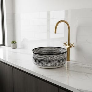 Round Moroccan ceramic vessel sink with hand-painted black-and-white geometric pattern and gold drain on a marble counter.