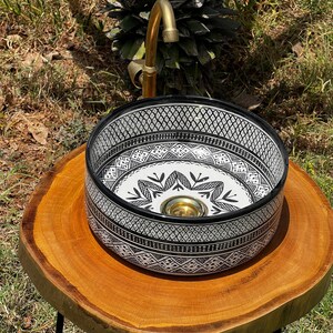 Round Moroccan ceramic vessel sink with hand-painted black-and-white geometric pattern and gold drain on a marble counter.