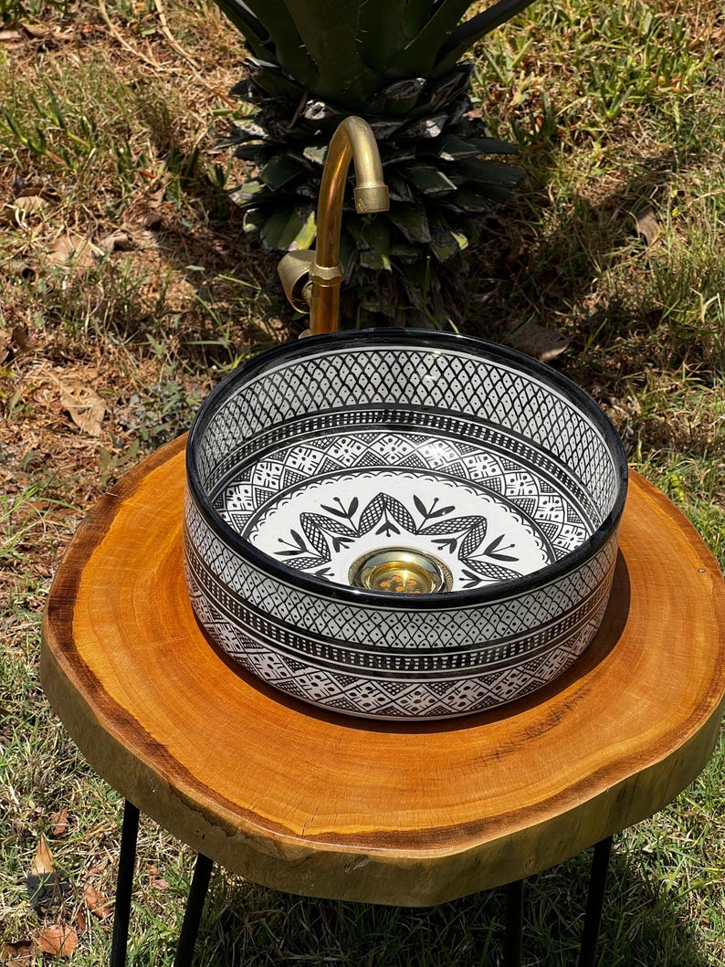 Round Moroccan ceramic vessel sink with hand-painted black-and-white geometric pattern and gold drain on a marble counter.