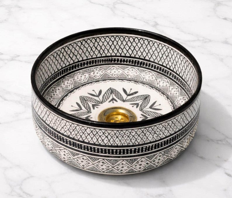 Round Moroccan ceramic vessel sink with hand-painted black-and-white geometric pattern and gold drain on a marble counter.