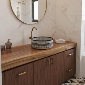 Round Moroccan ceramic vessel sink with hand-painted black-and-white geometric pattern and gold drain on a marble counter.