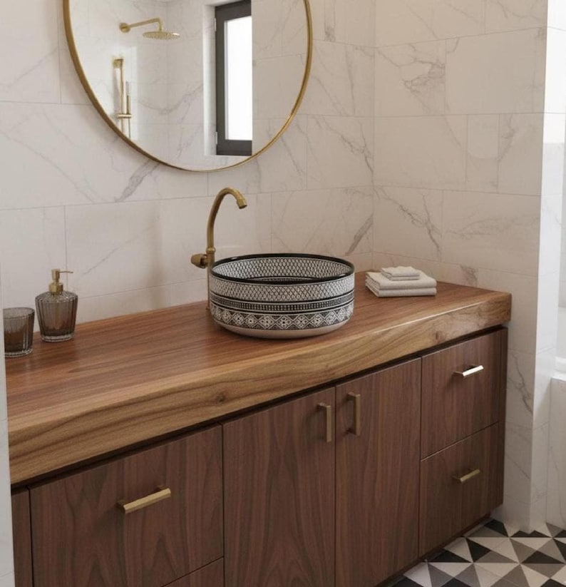 Round Moroccan ceramic vessel sink with hand-painted black-and-white geometric pattern and gold drain on a marble counter.