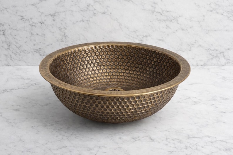 Custom made handmade brass sink: hammered copper bowl with rustic texture, tall luxe brass faucet on a wooden countertop.