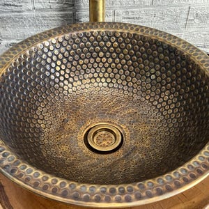 Custom made handmade brass sink: hammered copper bowl with rustic texture, tall luxe brass faucet on a wooden countertop.