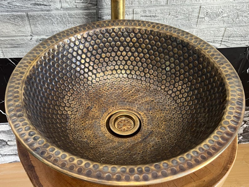 Custom made handmade brass sink: hammered copper bowl with rustic texture, tall luxe brass faucet on a wooden countertop.