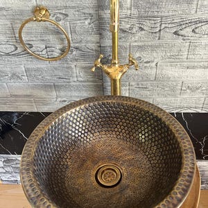 Custom made handmade brass sink: hammered copper bowl with rustic texture, tall luxe brass faucet on a wooden countertop.