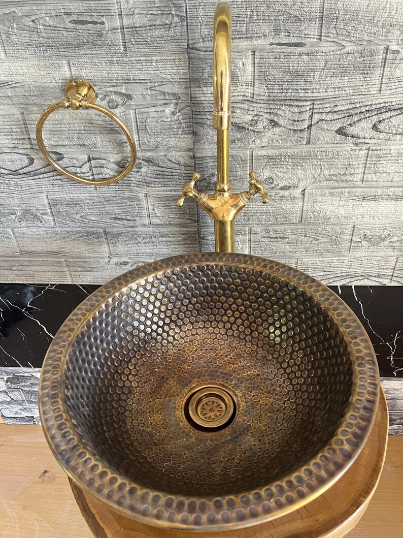 Custom made handmade brass sink: hammered copper bowl with rustic texture, tall luxe brass faucet on a wooden countertop.