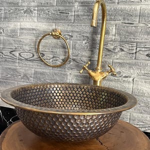 Custom made handmade brass sink: hammered copper bowl with rustic texture, tall luxe brass faucet on a wooden countertop.