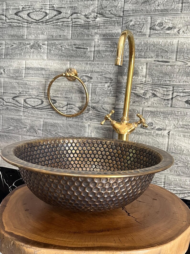 Custom made handmade brass sink: hammered copper bowl with rustic texture, tall luxe brass faucet on a wooden countertop.