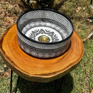 Round Moroccan ceramic vessel sink with hand-painted black-and-white geometric pattern and gold drain on a marble counter.