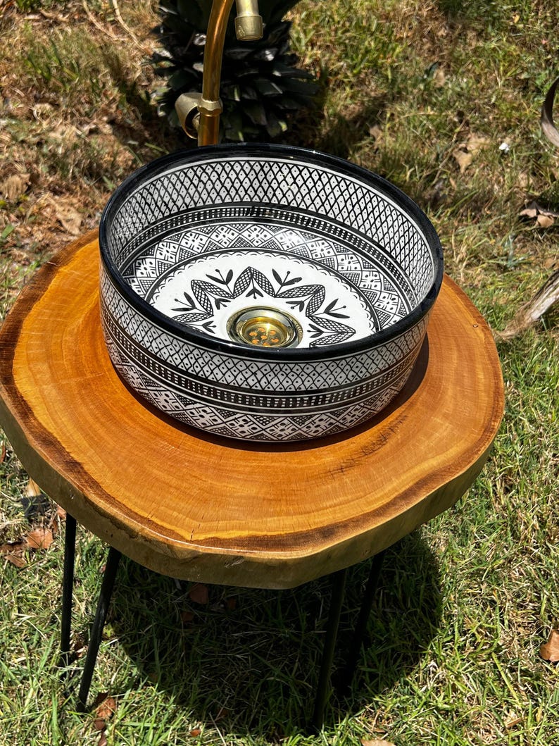 Round Moroccan ceramic vessel sink with hand-painted black-and-white geometric pattern and gold drain on a marble counter.
