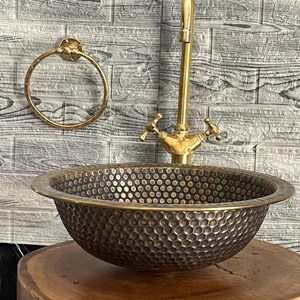 Custom made handmade brass sink: hammered copper bowl with rustic texture, tall luxe brass faucet on a wooden countertop.