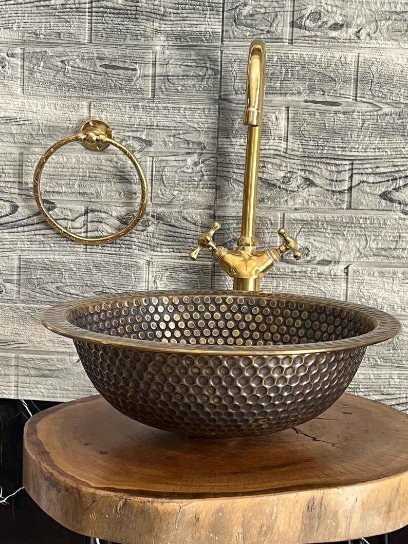 Custom made handmade brass sink: hammered copper bowl with rustic texture, tall luxe brass faucet on a wooden countertop.