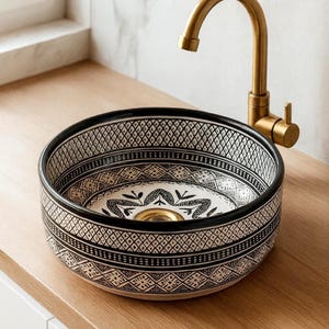 Round Moroccan ceramic vessel sink with hand-painted black-and-white geometric pattern and gold drain on a marble counter.