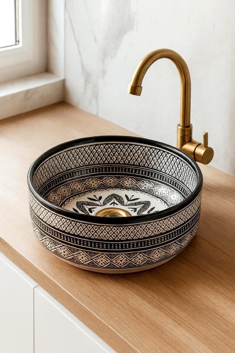 Round Moroccan ceramic vessel sink with hand-painted black-and-white geometric pattern and gold drain on a marble counter.