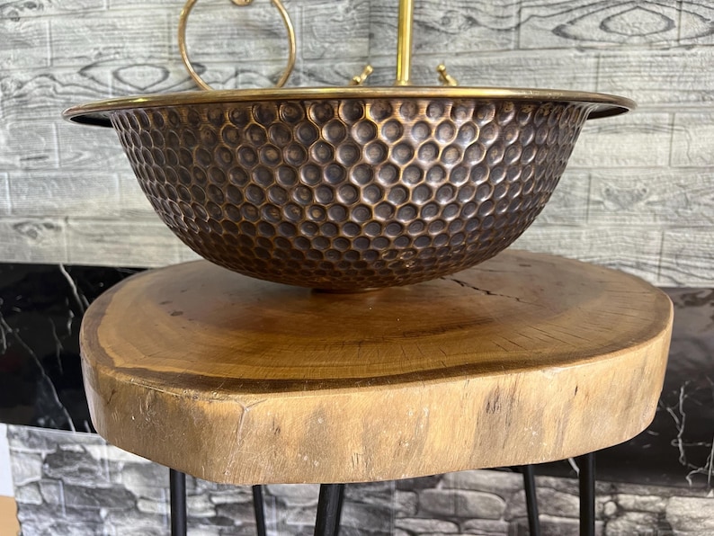 Custom made handmade brass sink: hammered copper bowl with rustic texture, tall luxe brass faucet on a wooden countertop.