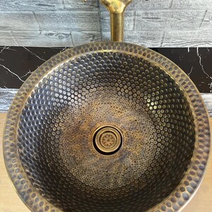 Custom made handmade brass sink: hammered copper bowl with rustic texture, tall luxe brass faucet on a wooden countertop.