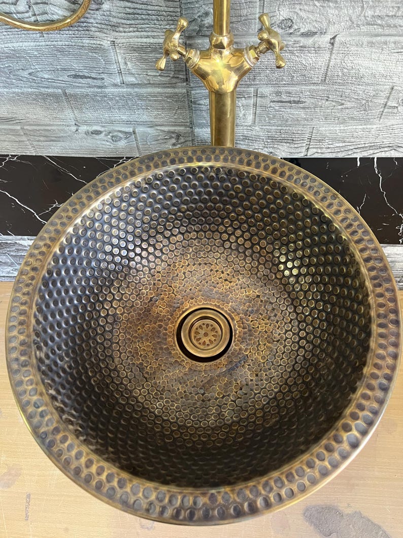 Custom made handmade brass sink: hammered copper bowl with rustic texture, tall luxe brass faucet on a wooden countertop.