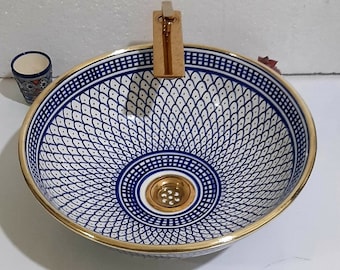 May include: A white ceramic bathroom sink with a blue and gold geometric pattern. The sink has a gold-coloured drain and a gold-coloured faucet.