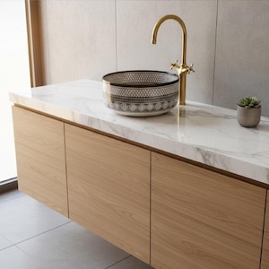 Round Moroccan ceramic vessel sink with hand-painted black-and-white geometric pattern and gold drain on a marble counter.