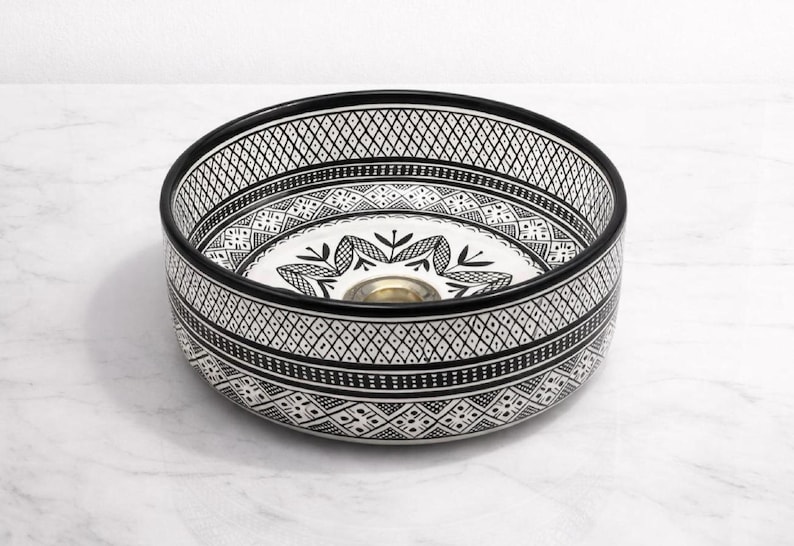 Round Moroccan ceramic vessel sink with hand-painted black-and-white geometric pattern and gold drain on a marble counter.