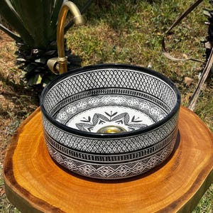 Round Moroccan ceramic vessel sink with hand-painted black-and-white geometric pattern and gold drain on a marble counter.