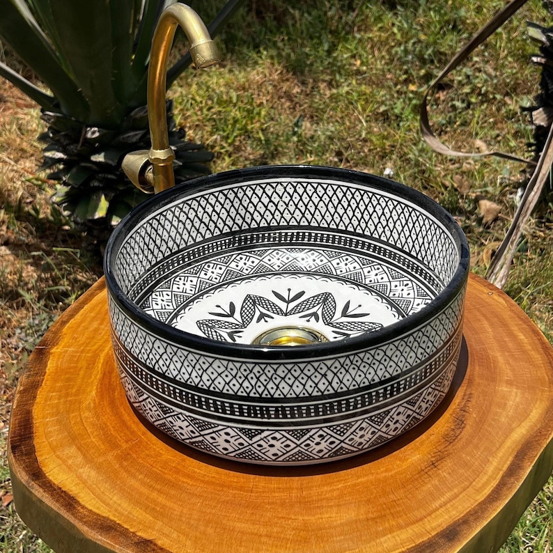 Round Moroccan ceramic vessel sink with hand-painted black-and-white geometric pattern and gold drain on a marble counter.