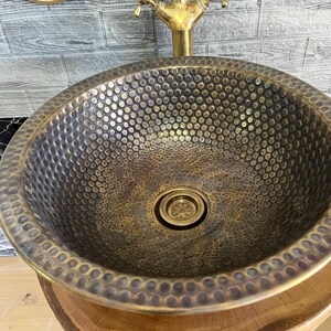 Custom made handmade brass sink: hammered copper bowl with rustic texture, tall luxe brass faucet on a wooden countertop.