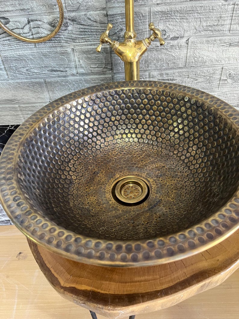 Custom made handmade brass sink: hammered copper bowl with rustic texture, tall luxe brass faucet on a wooden countertop.