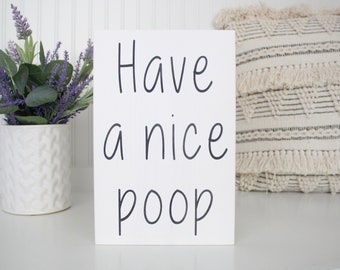 May include: White wooden sign with black handwritten text that reads "Have a nice poop".