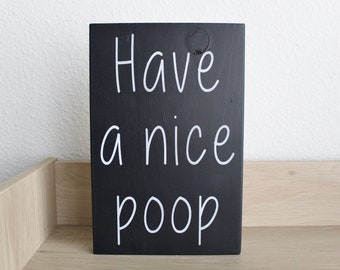 May include: Black wooden sign with white text that reads "Have a nice poop".
