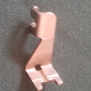 May include: A copper-colored metal bracket with a unique shape, featuring two small prongs on the top and a larger prong on the bottom.