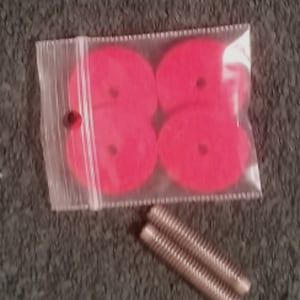 May include: Four bright pink, round, plastic discs with a small hole in the center, packaged in a clear plastic bag. Two silver metal screws are also included.