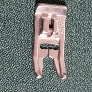 May include: A silver sewing machine foot with a metal shank and a small opening in the center. The foot is marked with the number "3/4".