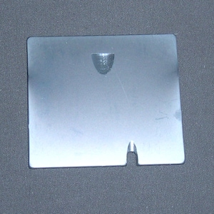 May include: A silver metal plate with a small hole in the center and a larger cut-out on the bottom edge.