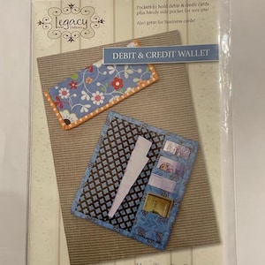 Puede incluir: Un paquete que presenta una cartera de tela azul y marrón con bolsillos para tarjetas de débito y crédito. La cartera se muestra con un tarjetero a juego con estampado floral. El texto en el paquete dice "DEBIT & CREDIT WALLET."