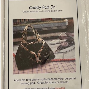 May include: A black and brown patterned tote bag with a handle, labeled "Caddy Pad Jr." The tote opens to become an ironing pad. The text says it is sized to hold a 6"-8.5" travel iron. The image also shows an iron and fabric.