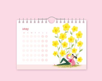 Pode incluir: Um calendário para o mês de maio com fundo rosa. O calendário apresenta uma ilustração de uma pessoa relaxando entre grandes flores amarelas. A palavra "May" é impressa no topo do calendário.