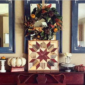 Puede incluir: Un tapiz de pared de madera con un patr&oacute;n de estrella roja, marr&oacute;n y blanca. El tapiz de pared se muestra en una superficie de madera oscura con una corona, calabazas y otra decoraci&oacute;n de oto&ntilde;o.