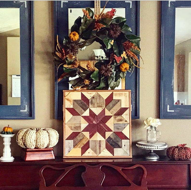 Puede incluir: Un tapiz de pared de madera con un patr&oacute;n de estrella roja, marr&oacute;n y blanca. El tapiz de pared se muestra en una superficie de madera oscura con una corona, calabazas y otra decoraci&oacute;n de oto&ntilde;o.
