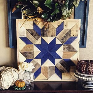 Puede incluir: Un tapiz de pared de madera con un patr&oacute;n geom&eacute;trico azul y marr&oacute;n. El patr&oacute;n est&aacute; formado por cuadrados y tri&aacute;ngulos, y crea una forma de estrella en el centro. El tapiz de pared est&aacute; enmarcado en madera y tiene un aspecto r&uacute;stico.
